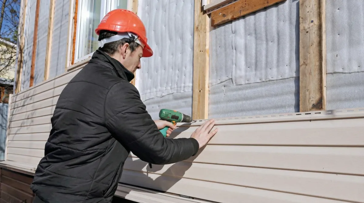 Siding replacement professional using a power drill to install new tan vinyl siding on a home exterior in Anaheim, CA